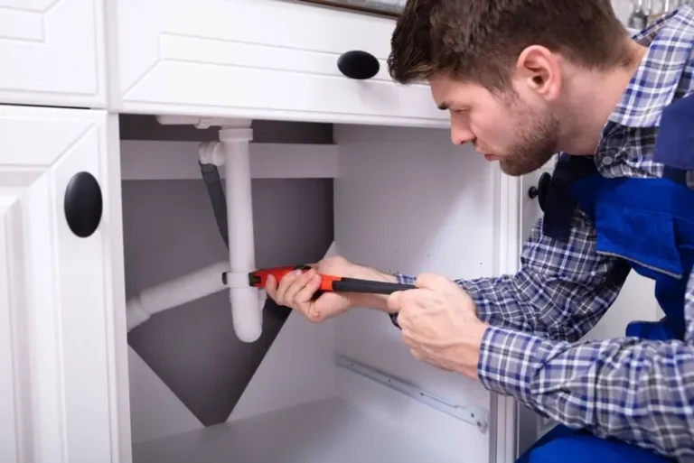 Plumber repairing bathroom sink plumbing under a cabinet in a residential property, emphasizing reliable plumbing service in Apache Junction AZ